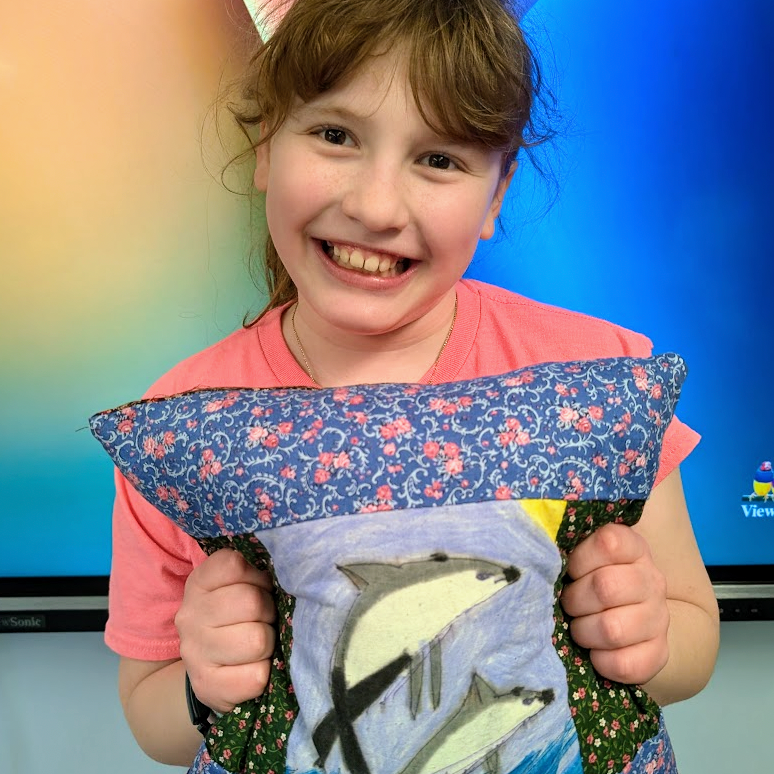 Student holds up pillow they sewed. 
